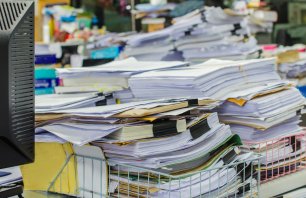 Pile of documents on desk stack up high waiting to be managed.