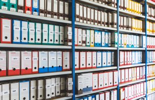 Detailed view of numerous shelves filled with folders of various colors. The folders are neatly arranged, showcasing an organized system for document storage. This image was taken in the ancient town hall of Ambronay small village, in Ain, Auvergne-Rhone-Alpes region in France.